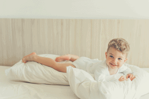 smiling toddler boy playing with pillows in bed