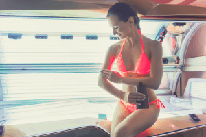 woman in bikini applying tanning lotion before lying in an indoor tanning bed